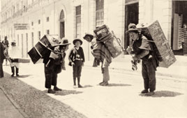 La Paz. Porters carrying trunks on their back on a street, between 1890 and 1923